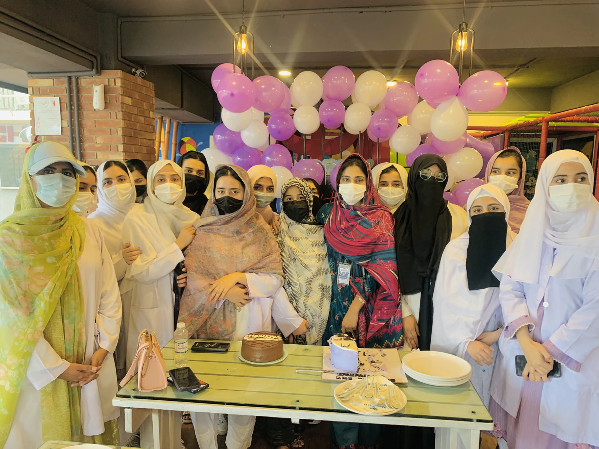 Students in white coats gathered around the cake at the ePreparians get-together